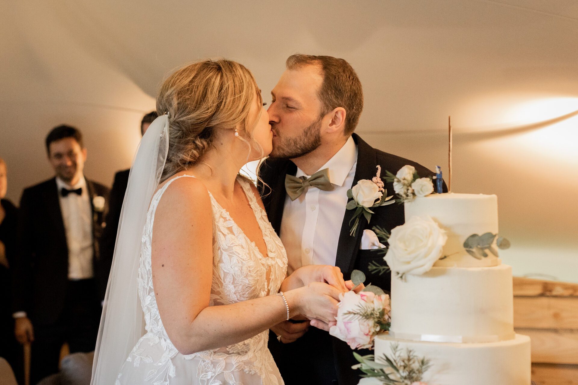 The bride and groom share a kiss as they cut the cake at Old Luxters Barn wedding venue in Oxfordshire