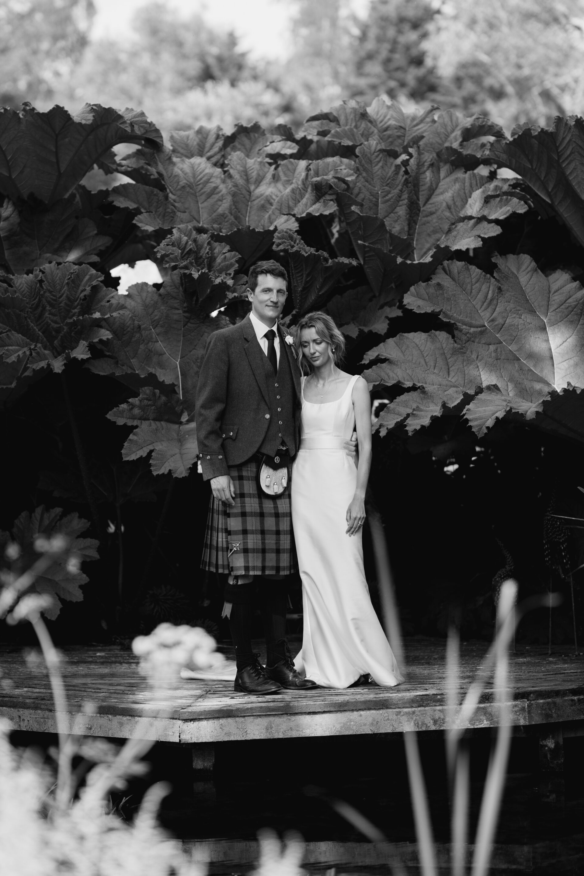 The bride and groom are framed by giant leaves during their couples portrait session
