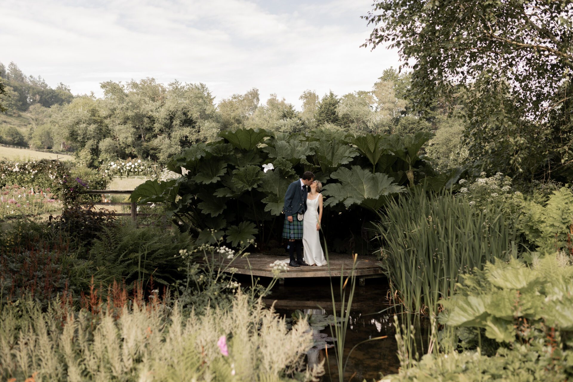 The bride and groom pose for a portrait next to a pond