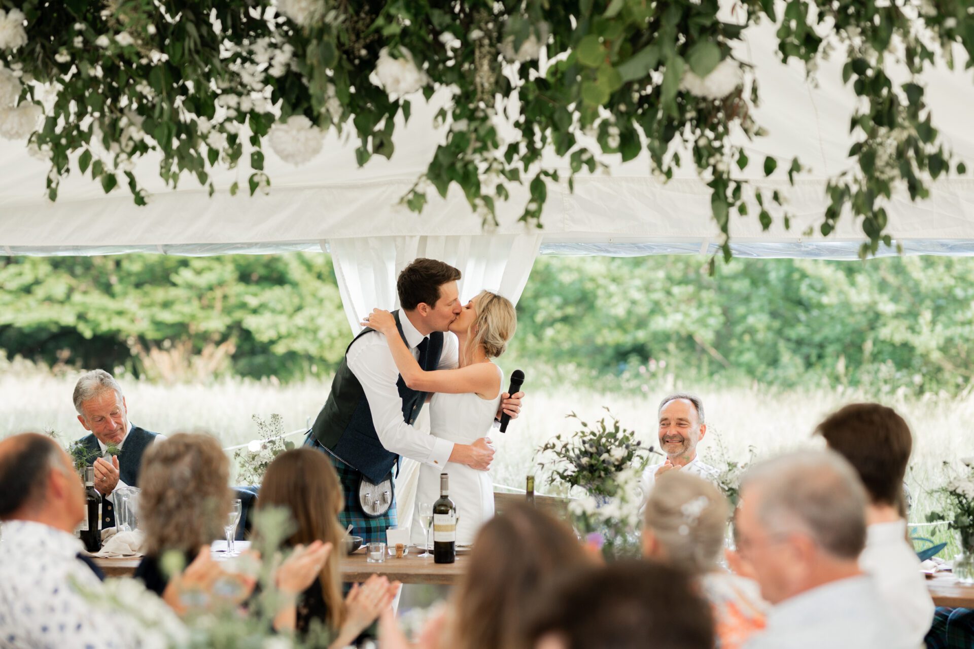 The bride and groom share a kiss during speeches at their Devon marquee wedding