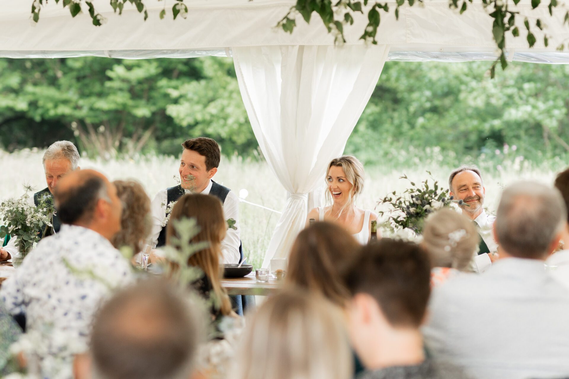 The bride and groom listen to speeches during their Devon marquee wedding