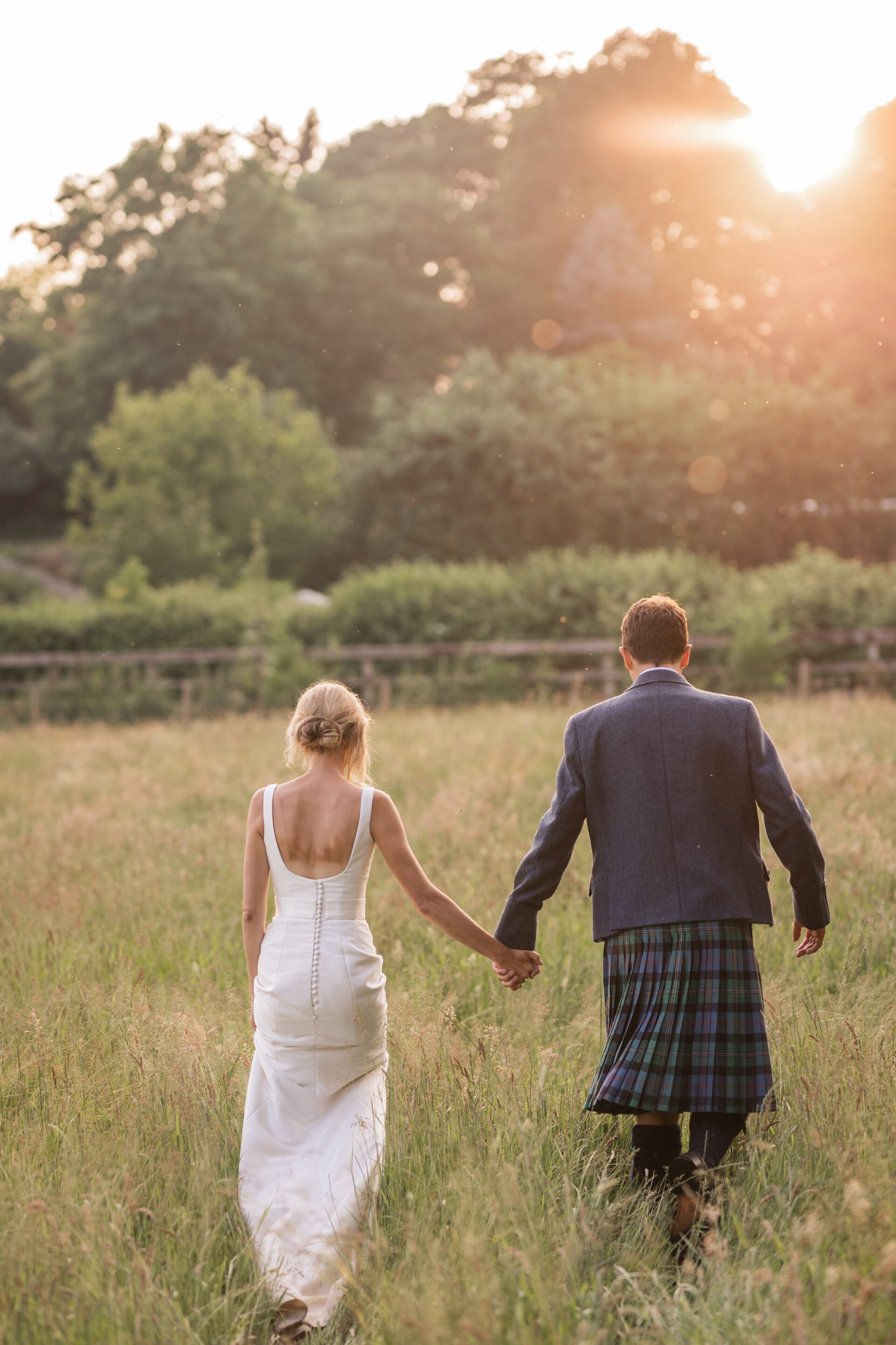 The bride and groom walk through the fields during golden hour