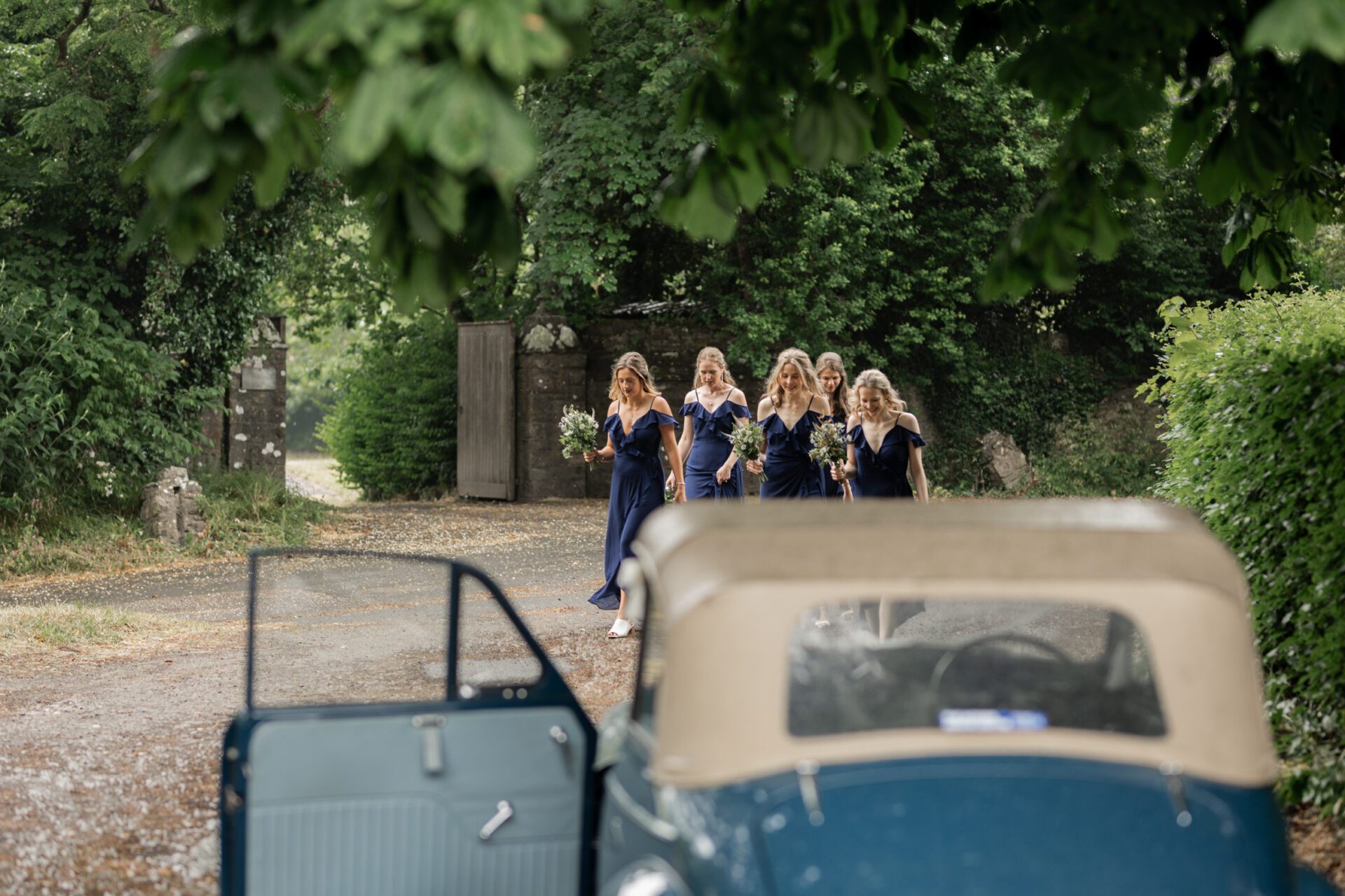 The bridal party await the bride as she exits the vintage wedding car