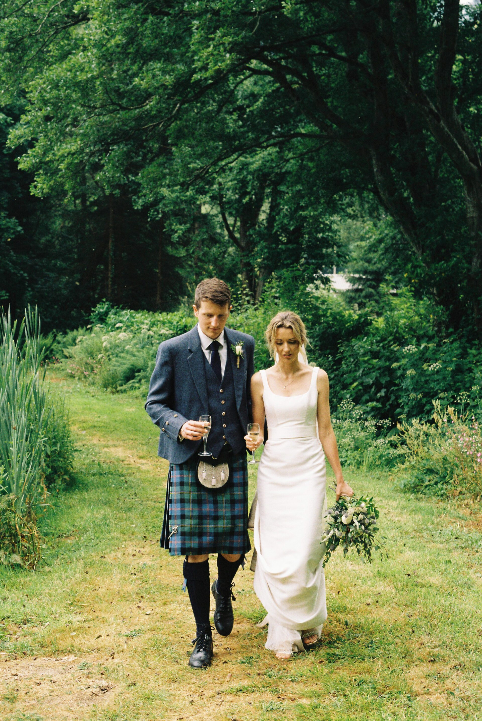 The bride and groom walk hand in hand, captured on 35mm film