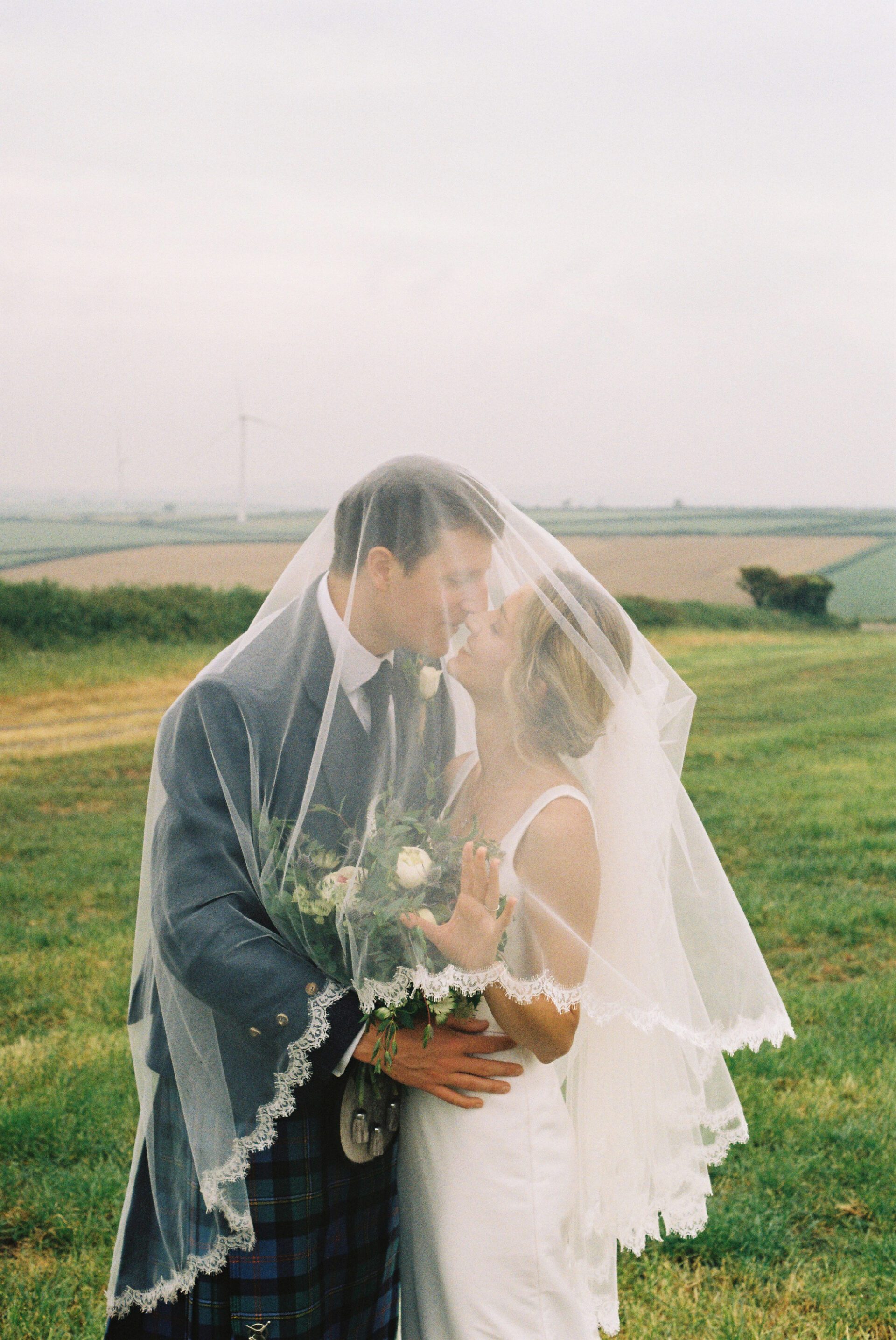 The bride and groom share a kiss beneath a veil, captured on 35mm film