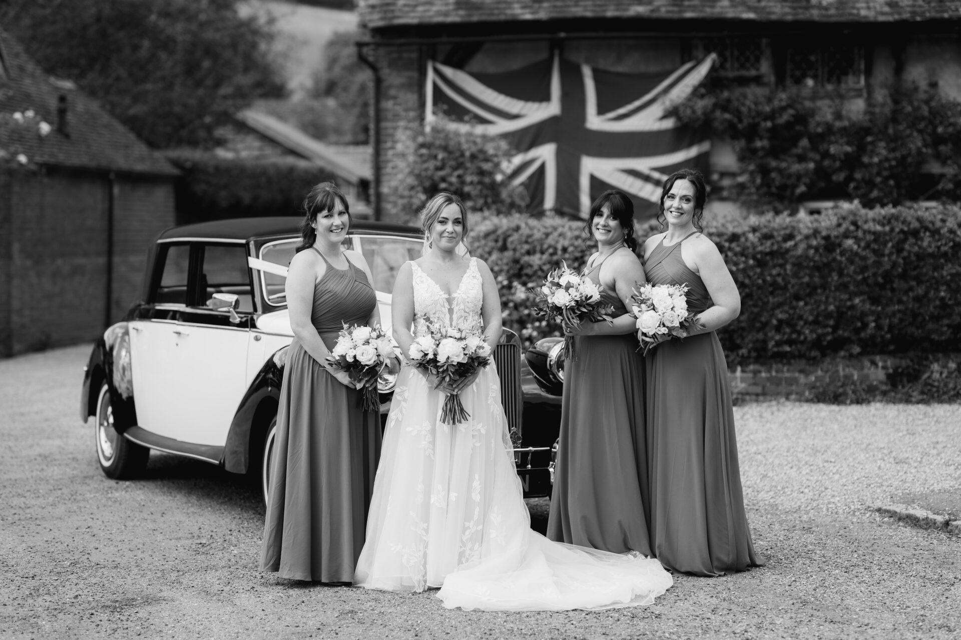 The bride stops for a photo with her bridesmaid in front of the vintage wedding car