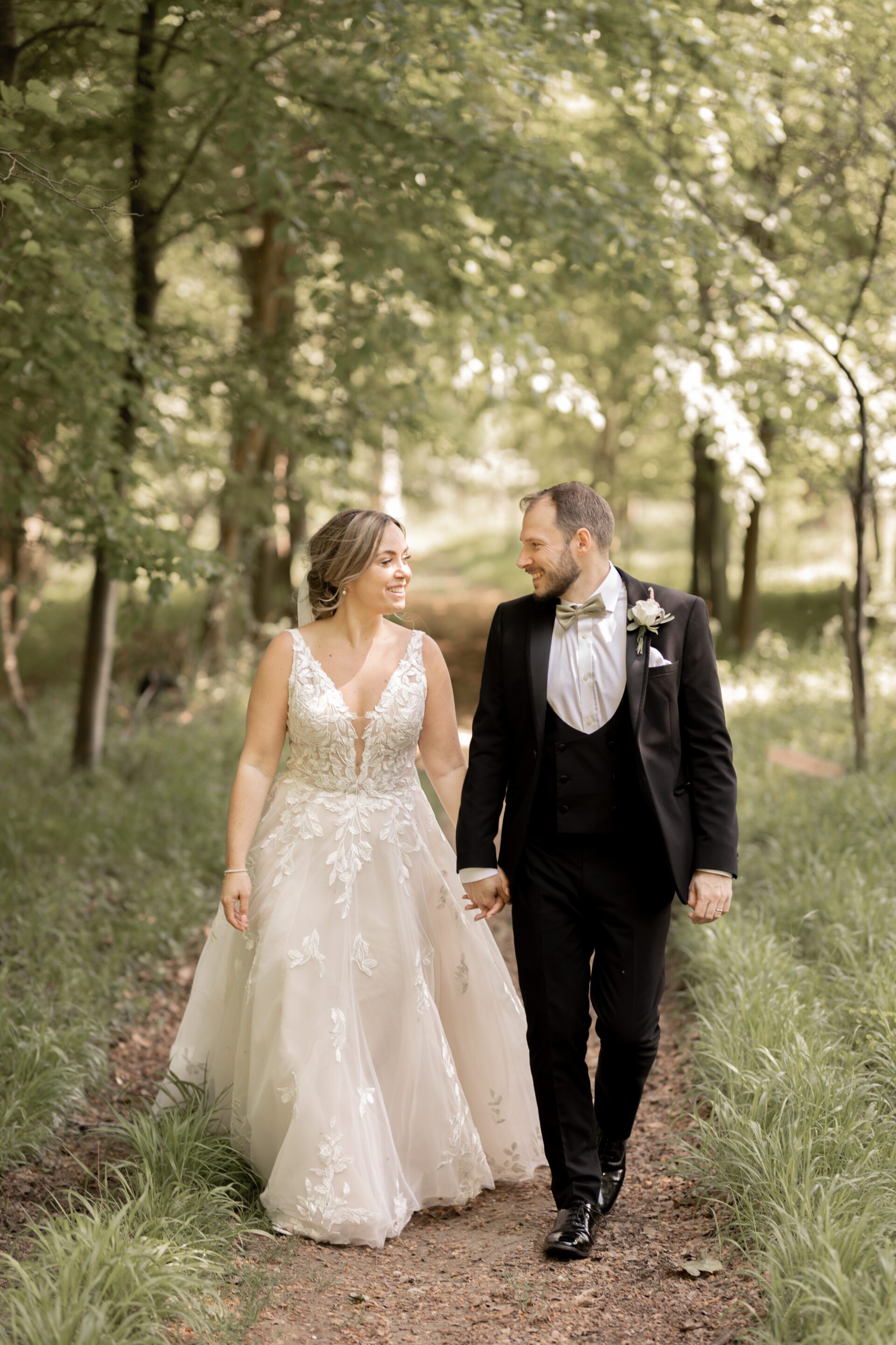 The bride and groom walk hand in hand through the woods at Old Luxters Barn in Oxfordshire