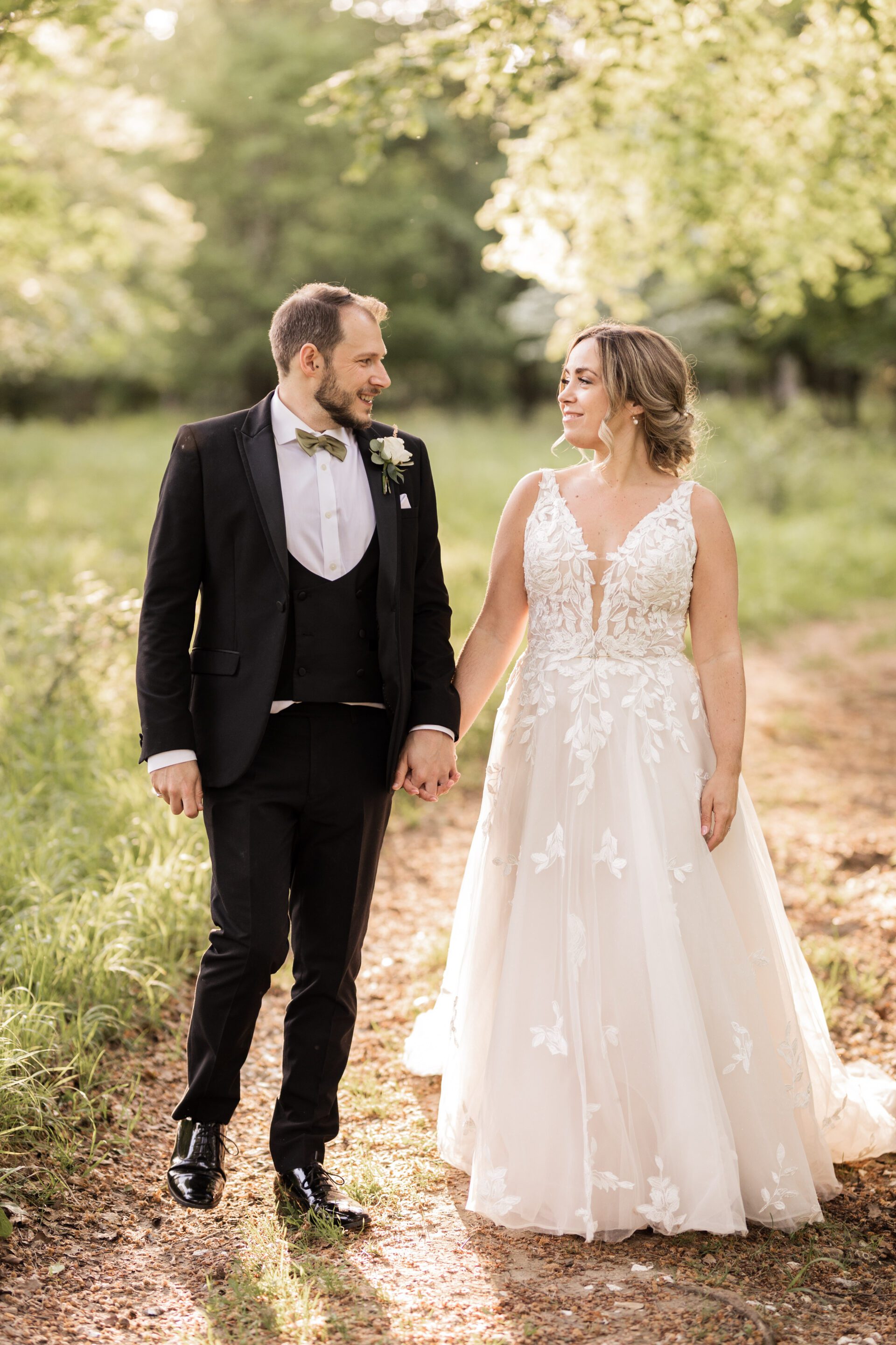 The bride and groom walk hand in hand during golden hour at their barn wedding