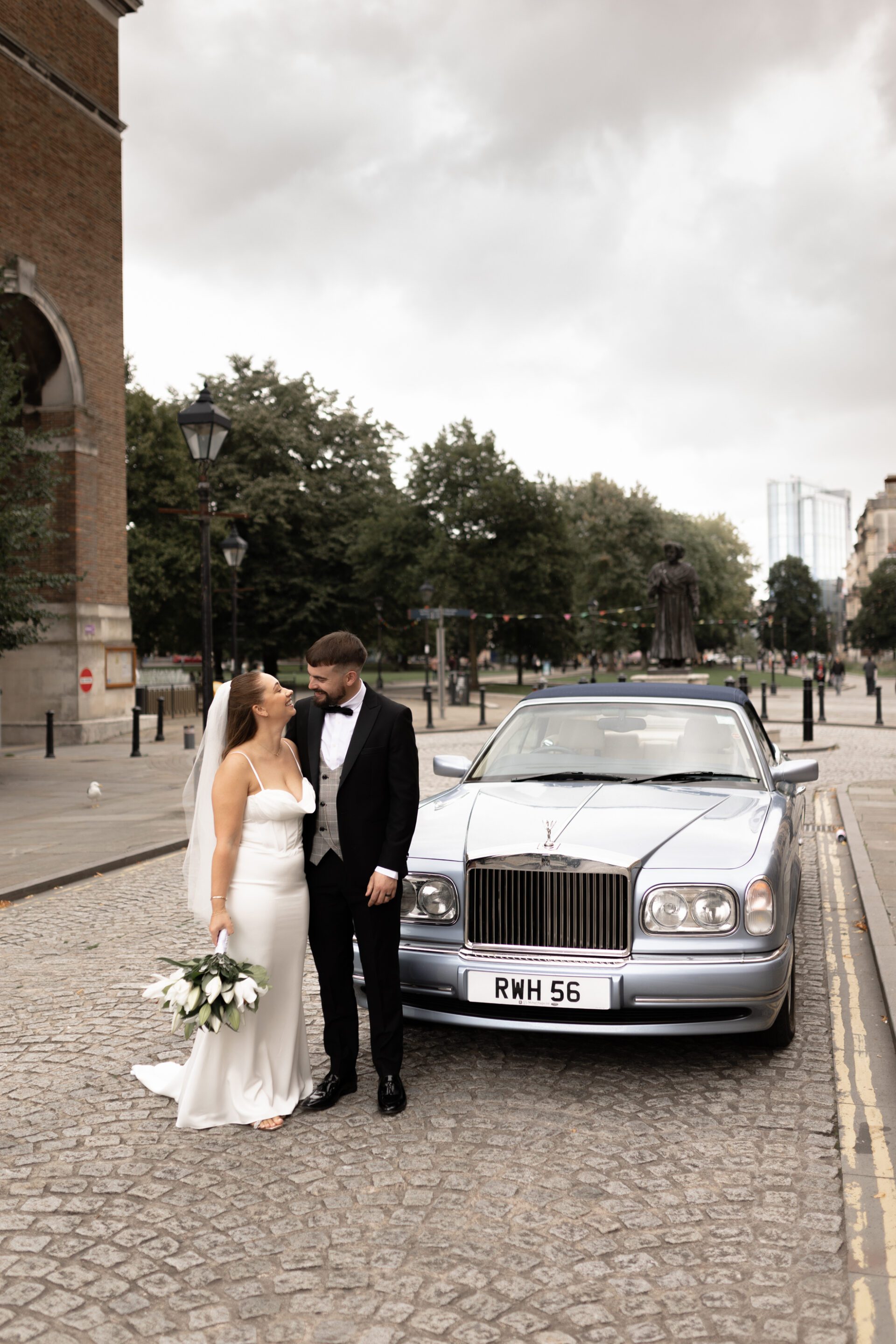 The bride and groom pose in front of their classic wedding car during their Bristol couple portrait session