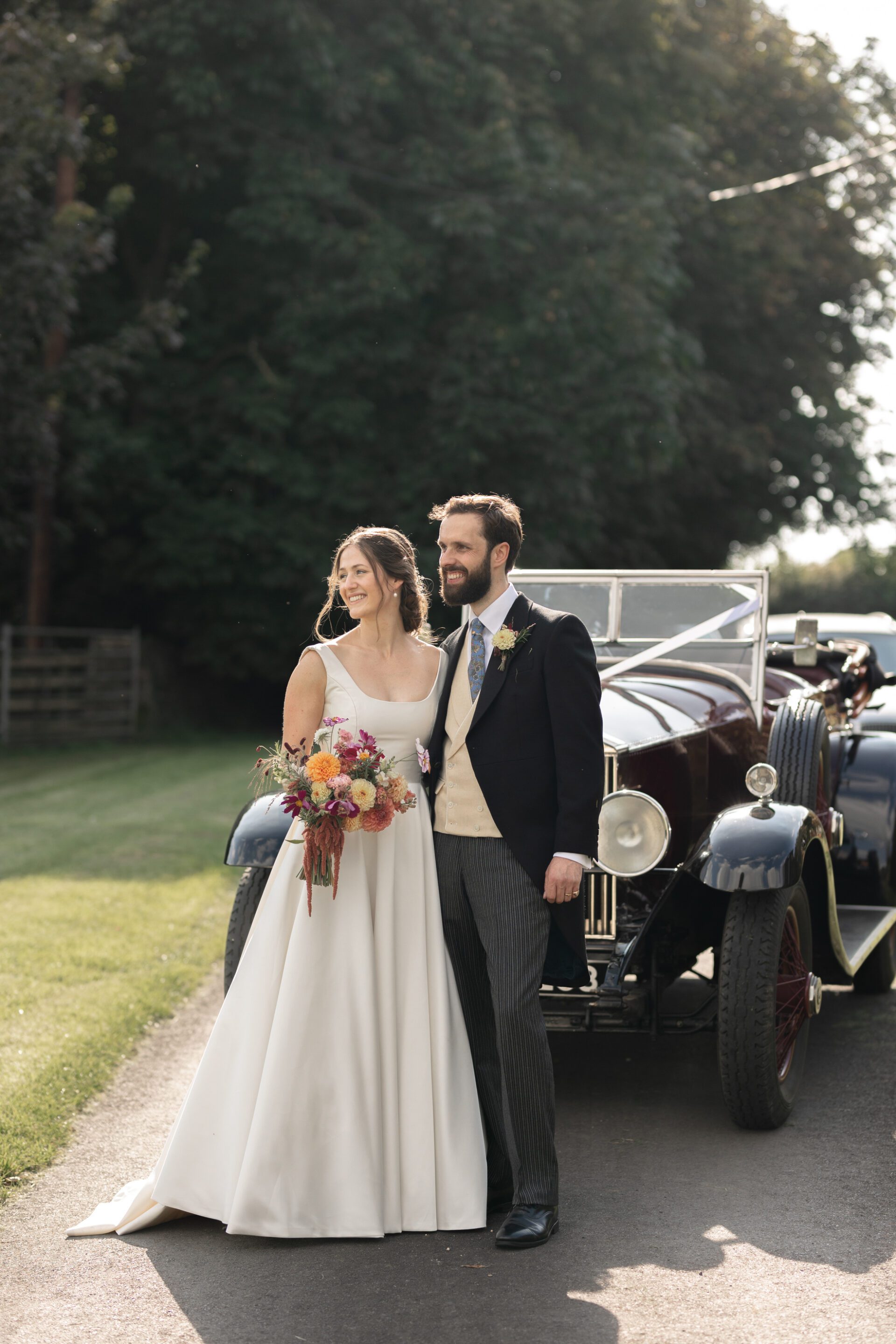 The bride and groom pose for a portrait in front of their vintage wedding car