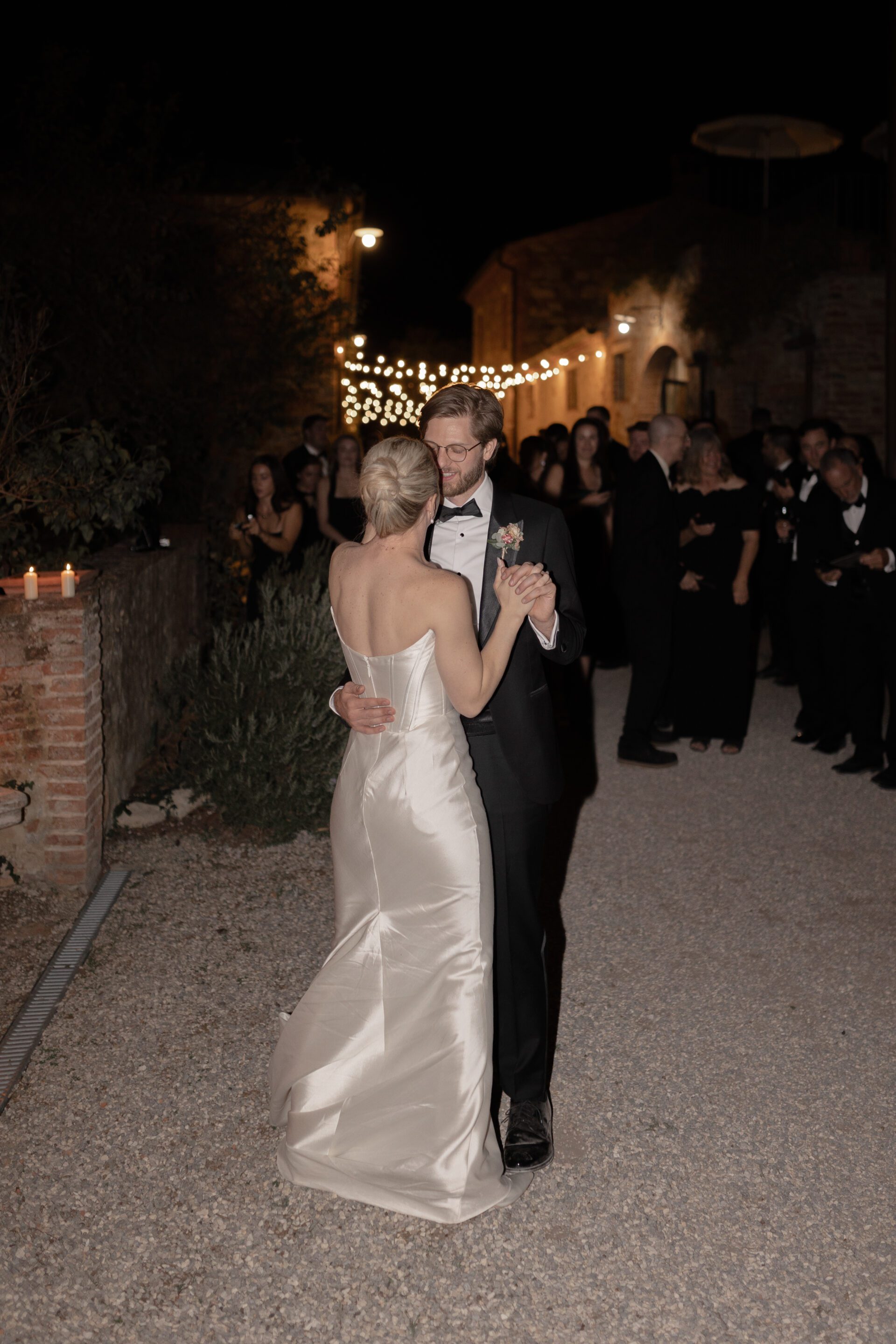 The bride and groom share their first dance in the Tuscan wedding venue courtyard surrounded by lights and candles